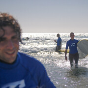 Uczestnik kursu uczy się surfingu w surfcampie Fuerteventura i uśmiecha się w płytkiej wodzie.