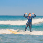 Surferka z powodzeniem staje na desce i płynie na białej fali podczas kursu dla początkujących.