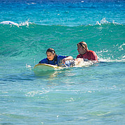 Instruktor surfingu popycha surfującego studenta do fali
